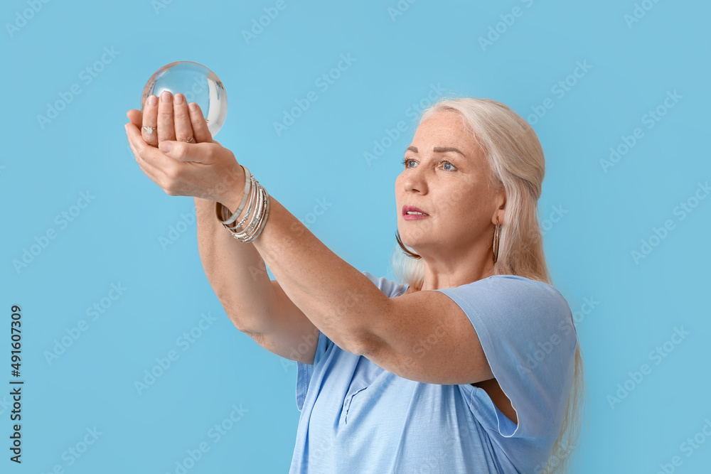 Mature woman with crystal ball on color background