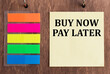 © Volha - a card with the text BUY NOW PAY LATER on a wooden background next to colored stickers