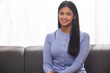 © IndiaPix - Young woman looking at camera while sitting on sofa in living room