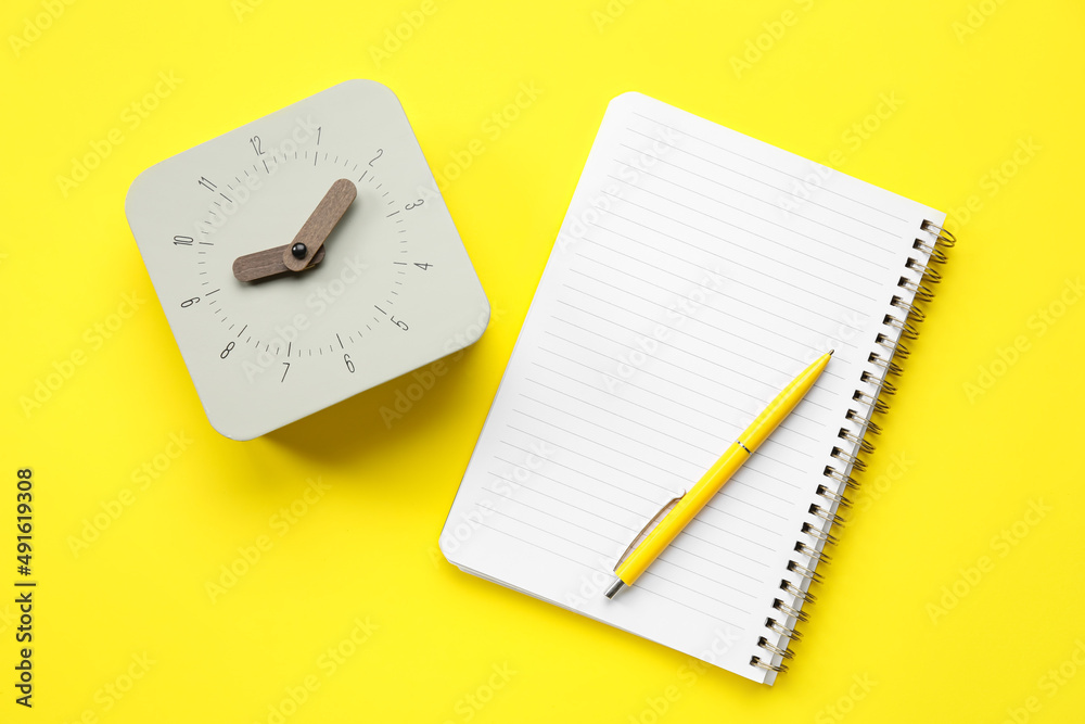 New alarm clock with notebook and pen on yellow background