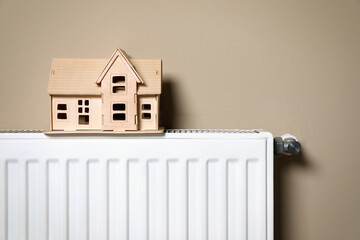 Wall Mural - Modern radiator with wooden house near beige wall indoors. Winter heating efficiency