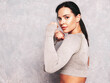 © halayalex - Fitness confident woman in sports clothing. Sexy young beautiful model stands in a rack. Female posing near grey wall in studio. She practice power punches, boxing during workout process