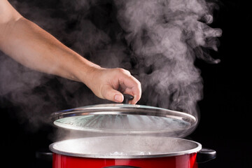 The chef's hand opens the lid of the hot soup pot. with smoke on black background for people cooking and boiling water in kitchen