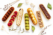 A lot of french dessert eclairs with colorful topping
