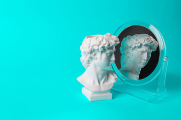 Bust of David admires himself looking in a mirror on turquoise background. Narcissism. Minimal still life