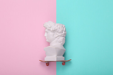 Wall Mural - David bust ride on skateboard, pink blue background. Creative layout. Minimal still life. Flat lay. Top view