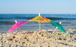 © mari1408 - Three small paper cocktail umbrellas stand in sand on sandy beach close-up. Small paper umbrellas on sandy shore near sea and sea waves on sunny summer day. Leisure, Vacation, Travel, Tourism Concept