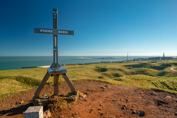 Iron cross on top of Pinneberg, the highest point of the island of Helgoland. Beautiful sunny day of winter in German archipelago with Northern sea and Dune island in the back.