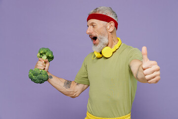 Wall Mural - Elderly gray-haired bearded man 40s years old in headband khaki t-shirt hold broccoli dumbbell show thumb up like gesture look aside isolated on plain pastel light purple background studio portrait.