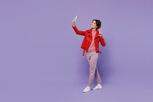 Full Body Young Smiling Happy Woman 20s Wear Red Leather Jacket Doing Selfie Shot On Mobile Cell Phone Post Photo On Social Network Isolated On Plain Pastel Light Purple Background Studio Portrait