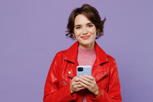 Young Smiling Happy Fun Woman 20s Wear Red Leather Jacket Hold In Hand Use Mobile Cell Phone Chatting Online Isolated On Plain Pastel Light Purple Background Studio Portrait. People Lifestyle Concept.
