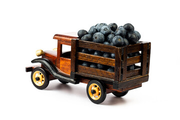 Brown wooden toy truck with ripe blueberry on white background.