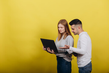 Happy girl with boyfriend looking at laptop on yellow background. They study together. Solve problems. Learning work concept