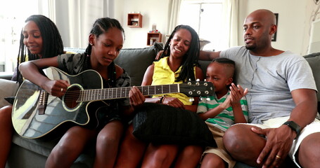 Canvas Print - African daughter playing guitar together with family at home sofa