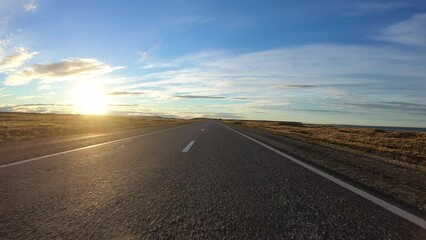 Sticker - Point of view of a car driving along the asphalt road in the yellow field at sunset.