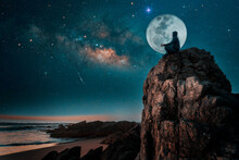 Person Silhouette Sitting On The Top Of The Mountain Meditating Or Contemplating The Starry Night With Milky Way And Moon Background.