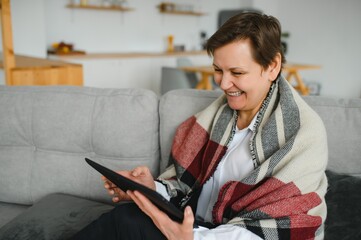 Sticker - Middle-aged woman reading a message, e-book or information on her tablet computer with a look of excited anticipation as she sits on a couch at home