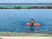 A Little Boy In The Pool Swims In Armlets And Lets Out A Jet Of Water From His Mouth