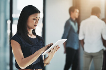 Theres an app for everything nowadays. Shot of a young businesswoman using her digital tablet in a modern office with her colleagues in the background.