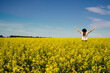 © Margarita Timofeeva - the woman in the hat enjoying nature in the middle of field full of yellow flowers. Yellow field of flowering rapeseed with cloudy blue sky - brassica napus - plant for green energy, medicine.