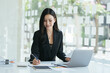© PaeGAG - Smiling young asian businesswoman taking notes while sitting with laptop computer over white background