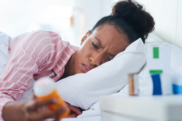 Sticker - I wonder if these pills will help me feel better. Shot of an attractive young woman holding a bottle of pills in bed at home.