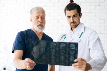 Wall Mural - Portrait of senior aged surgeon and young radiologist doctor discussing together history disease of patient using MRI scan of head in hospital office. Concept of modern medicine and health care.