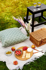 Wall Mural - leisure, food and drinks concept - close up of snacks, wine and picnic basket on blanket on grass