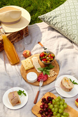 Wall Mural - leisure, food and drinks concept - close up of snacks and picnic basket on blanket on grass at summer park