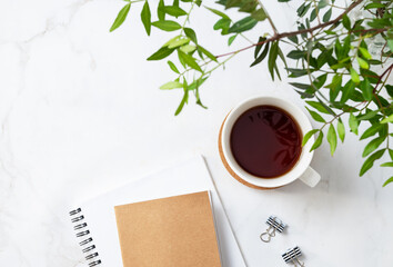 Wall Mural - A cup of tea and craft notepad  on a light marble background with green branches close-up. Spring women's concept. Top view and copy space