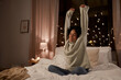 © Syda Productions - winter, comfort and people concept - happy smiling woman in woolen high neck sweater stretching in bed at home at night