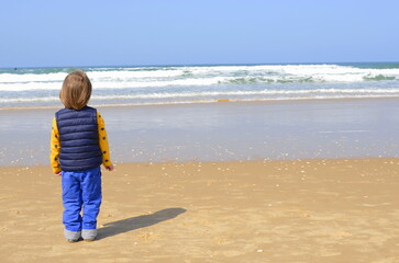 Little boy, age three. Standing with his back to the camera, looking at the sea. Skyline.