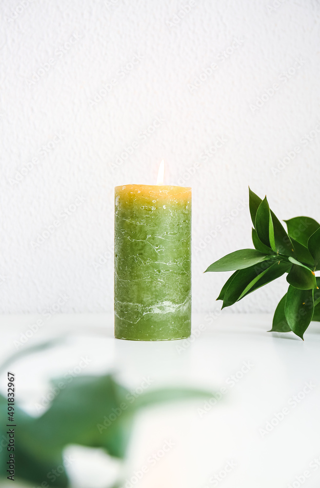 Burning green candle on white shelf