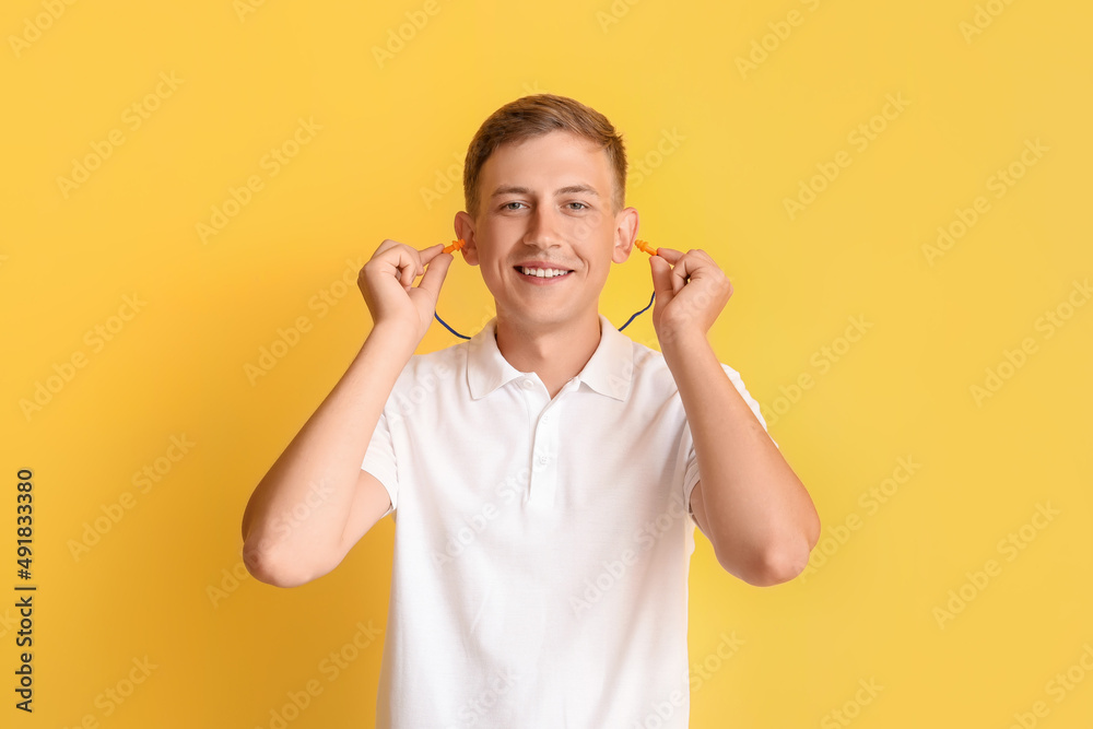 Handsome young man inserting earplugs on yellow background