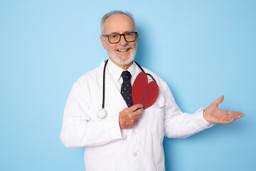 Wall Mural - Senior age handsome grey-haired doctor man holding heart of red paper with a happy face standing and smiling with a confident smile showing teeth. Medical concept.