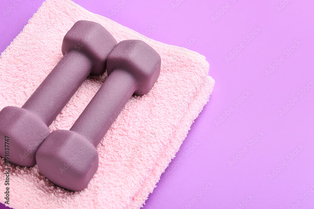 Stylish dumbbells and towel on purple background