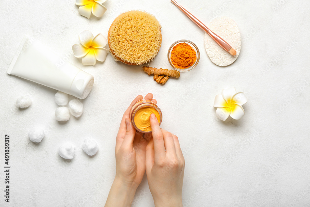 Female hands with jar of turmeric mask on light background