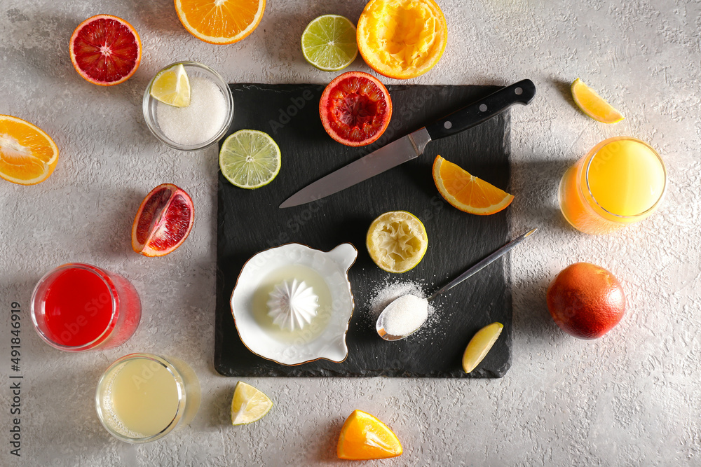 Ceramic juicer, juice, sugar and citrus fruits on grey background