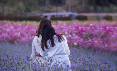 Two women hugging while watching sunset in the middle of Lavender and Cosmos field.  LGBT or friend love concept.