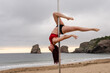Young caucasian girl doing pole dance at sunrise at a beautiful beach. Acrobatics of pole dance face down on the sand of the beach of Hendaya, France