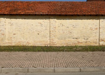 Old grunge yellow brick wall with terracotta tiled roof. A stripe of grass and concrete tiled sidewalk in front. Background for copy space