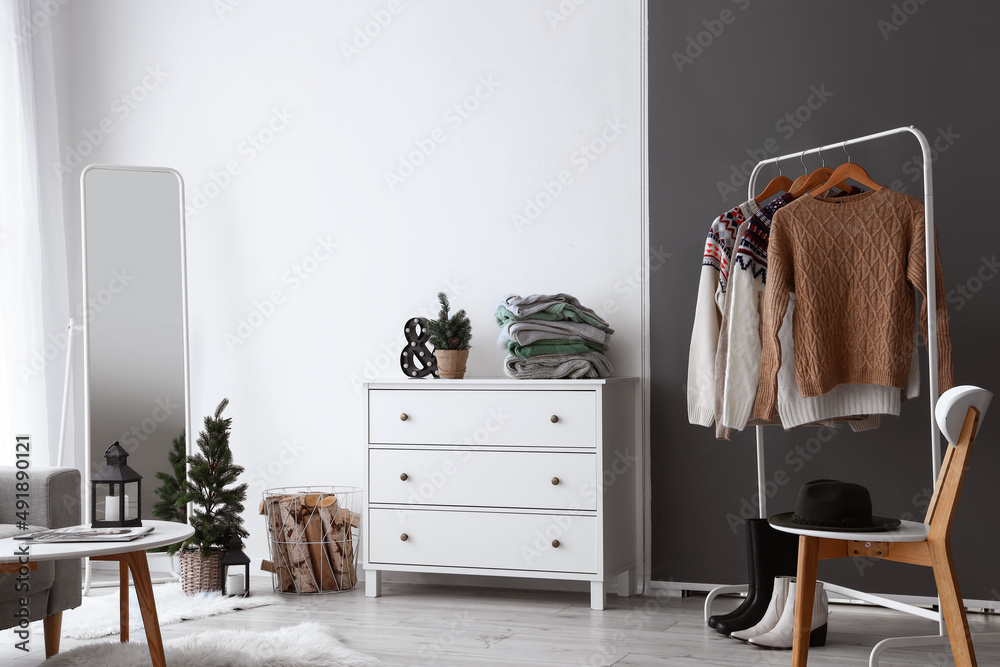 Interior of light living room with commode, rack and warm sweaters
