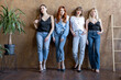 © rh2010 - Portrait of four diverse girlfriends standing together on the wall background indoors. Concept of female friendship and beauty. Women with different hair color wearing casual jeans