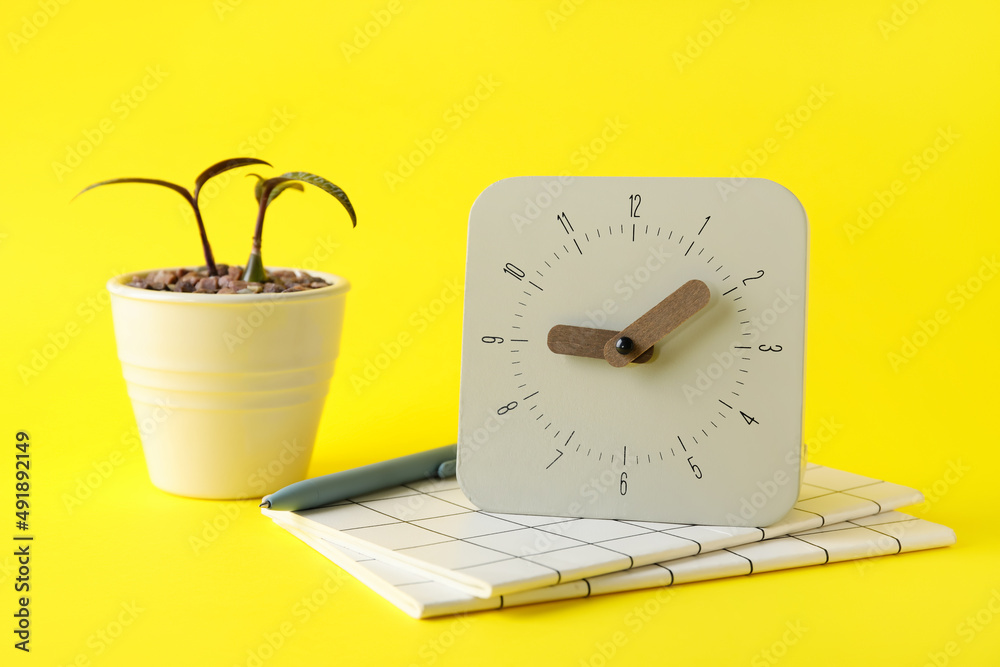 New alarm clock with houseplant and notebooks on yellow background