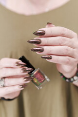 Female hand with long nails and a bottle of brown green nail polish