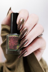 Female hand with long nails and a bottle of brown green nail polish