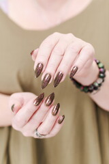 Female hand with long nails and a bottle of brown green nail polish