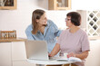 © Andriy Medvediuk - young woman teaching senior mother to use internet on laptop at home. daughter helps her elderly mother figure it out online with her personal account, teaches at modern gadget indoors.