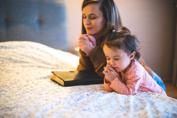 Wall Mural - Mother and her daughter reading from bible and praying in their knees near the bed