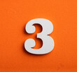 Three, white wooden number on orange background